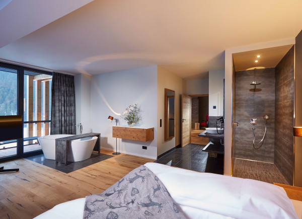 Blick vom Bett auf die freistehende BAdewanne vor der großen Fensterfront, alles sehr modern