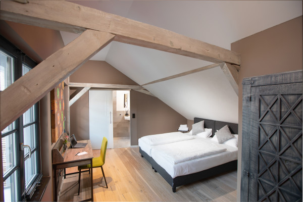 Schlafzimmer mit großem Bett unter der Dachschräge mit freigelegtem Bebälk